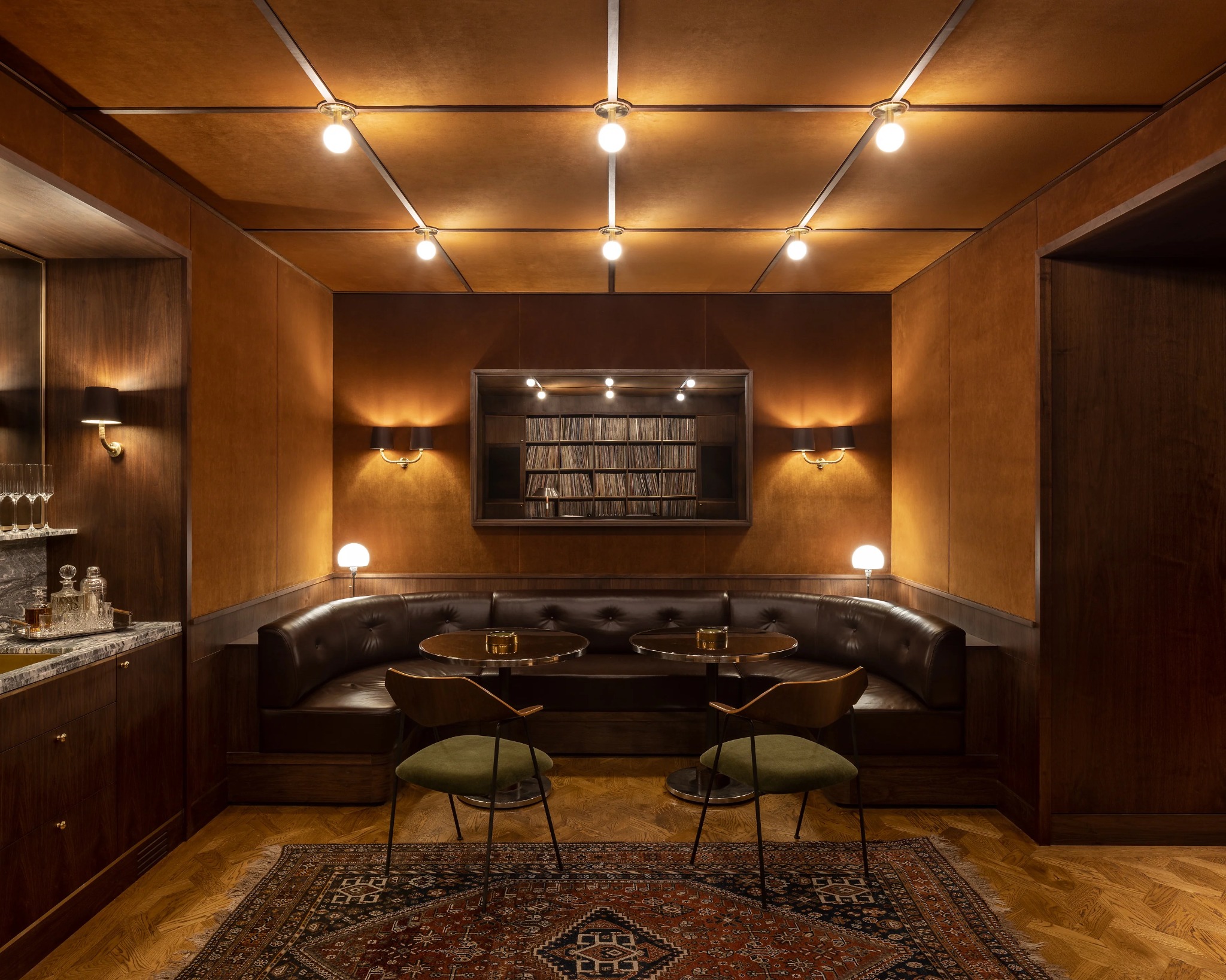Warmly lit private lounge with leather banquette, marble bar and record collection
